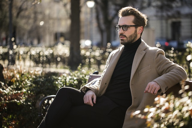 Man with a short beard sitting on a bench in the sun.