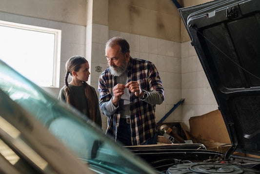 Man with a beard talking to daughter in garage while fixing a car